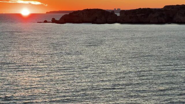 Beautiful sandy beach with red rocks and cliffs. Sunset at dusk with shallow waves on the Atlantic coast in Praia do Po&ccedil;o Velho, Praia da Fal&eacute;sia, Algarve, Portugal
