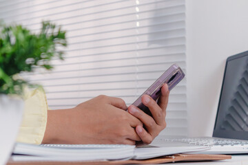 A businesswoman using smartphone and laptop at her desk