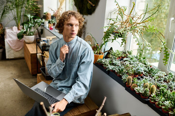 Creative young man working on a laptop surrounded by plants in a bright space