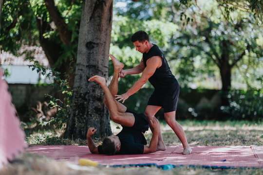 Two men train in wrestling on a red mat in a park, practicing holds and balance under trees. Outdoor fitness and teamwork showcase strength, focus, and athletic effort. - Powered by Adobe