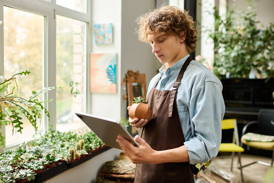 Creative young man nurturing plants while using a tablet in a bright indoor garden space - Powered by Adobe