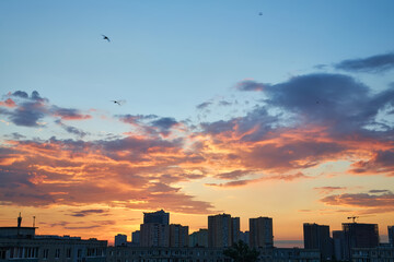 Fototapeta premium Sunset sky over a city skyline with buildings under construction.