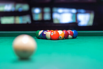 A single, white cue ball rests on a vibrant green pool table felt in a dimly lit setting, with a...