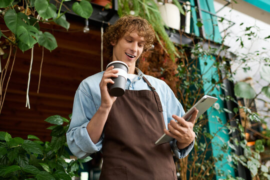 Young creative man enjoying a coffee while working on a tablet in a lush urban cafe space