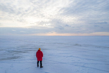 A lone person in a red jacket on a vast, frozen, snow-covered plain.