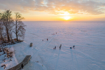 People enjoying a winter sunset on a vast frozen lake.