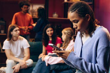Young woman engrossed in phone, feeling alone among friends at social gathering