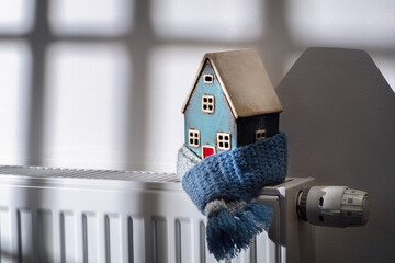 House model wrapped in scarf on radiator winter energy, heating and insulation background