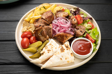 Shish kebab with potatoes, suluguni in lavash with ketchup in plate on the table