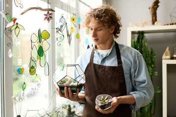 Creative young man showcasing unique terrariums in a bright workshop filled with greenery