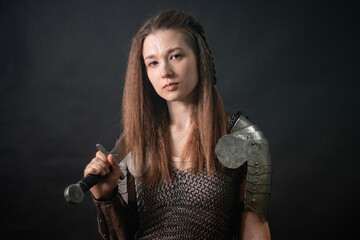 Obraz premium Portrait of a young woman, fantasy warrior in armor with a sword in her hands isolated on a dark background.