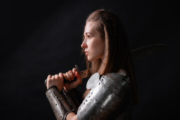 Obraz premium Portrait of a young woman, fantasy warrior in armor with a sword in her hands isolated on a dark background.