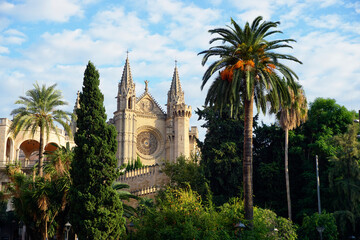 The Cathedral of Santa Maria of Palma in Palma de Mallorca, Spain. The view of the part of facade with twin spires and rose window and luxurious garden in the foreground