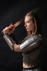 Obraz premium Portrait of a young woman, fantasy warrior in armor with a sword in her hands isolated on a dark background.