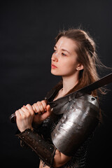 Obraz premium Portrait of a young woman, fantasy warrior in armor with a sword in her hands isolated on a dark background.