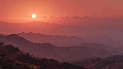 Fototapeta premium Sunset over layered mountains with an orange-pink sky and hazy silhouettes. Concept Sunset Landscape Photography, Layered Mountain Ranges, Orange-Pink Sky, Silhouettes at Dusk, Hazy Atmosphere