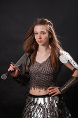 Fototapeta premium Portrait of a young woman, fantasy warrior in armor with a sword in her hands isolated on a dark background.