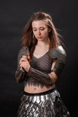 Fototapeta premium Portrait of a young woman, fantasy warrior in armor with a sword in her hands isolated on a dark background.