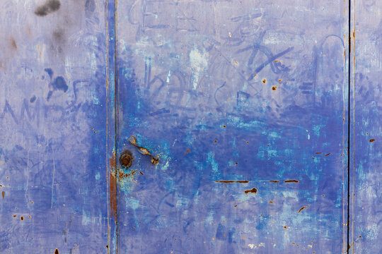 Close-up of weathered blue metal door with rust and graffiti