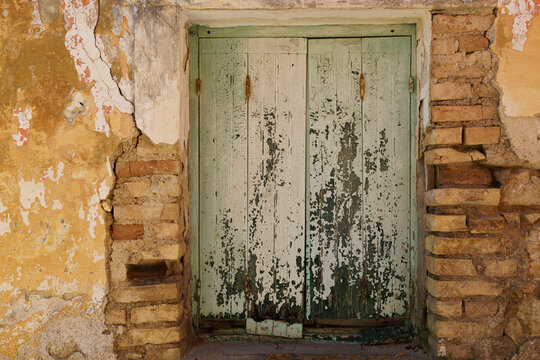 Pale green door in limestone wall with crumbling plaster