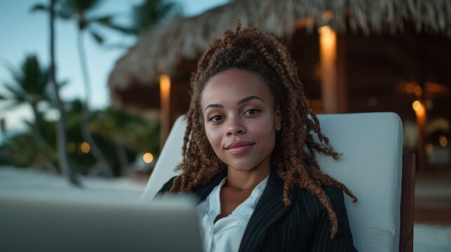 A confident woman sits at the beach, working on her laptop while enjoying the relaxing atmosphere, balancing productivity and leisure in a scenic tropical environment.