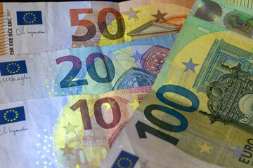 euro banknotes (100, 50, 20, 10) illuminated under ultraviolet light, revealing hidden security threads and fluorescent elements, representing european finance