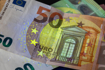 fifty euro banknote under powerful uv light, dramatically emphasizing the architectural window, stars, and yellow-green security features. european financial crisis concept