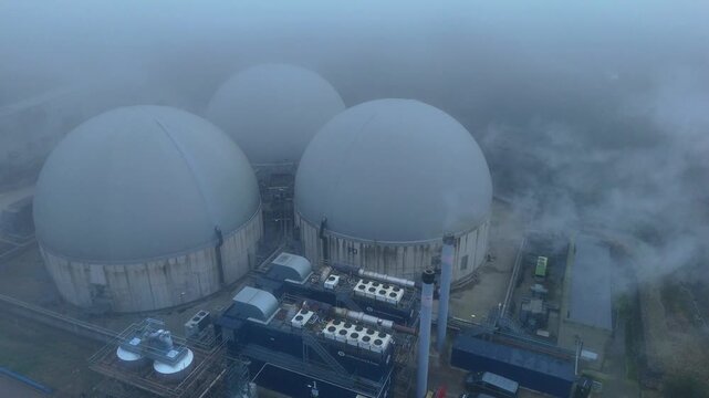 Aerial drone view of industrial factory domes, biogas generation production plant in foggy conditions with smoke stacks, Bury Saint Edmunds, UK