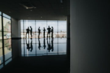 A group of silhouetted coworkers stand in a bright modern lobby, conversing near a glass wall.