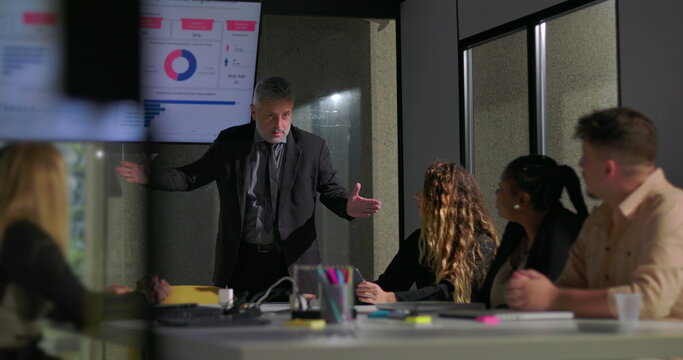 Corporate manager explaining report data to attentive colleagues in boardroom with screen displaying colorful charts and graphs - Powered by Adobe