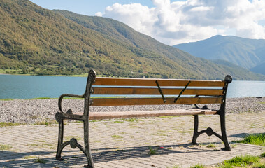 Secluded park bench by the lake surrounded by mountains on a sunny day