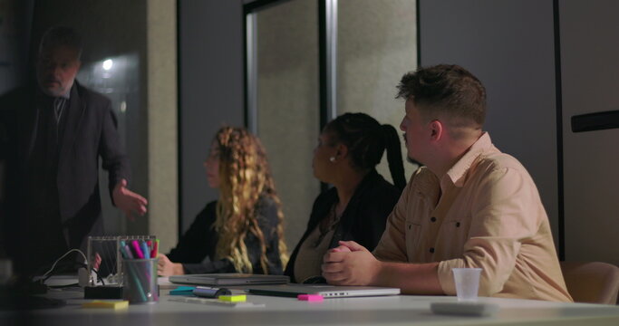 Corporate manager explaining report data to attentive colleagues in boardroom with screen displaying colorful charts and graphs