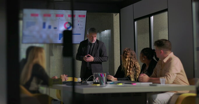 Corporate manager explaining report data to attentive colleagues in boardroom with screen displaying colorful charts and graphs - Powered by Adobe