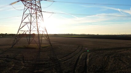 Aerial drone cinematic view of electricity pylons and powerlines silhouetted against winter sunset near UK power plant energy infrastructure landscape - Powered by Adobe
