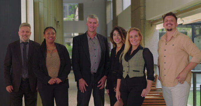 Corporate team smiling and standing together in office corridor, group of diverse professionals facing camera in relaxed and positive work environment - Powered by Adobe