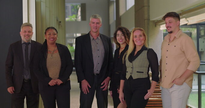 Corporate team smiling and standing together in office corridor, group of diverse professionals facing camera in relaxed and positive work environment