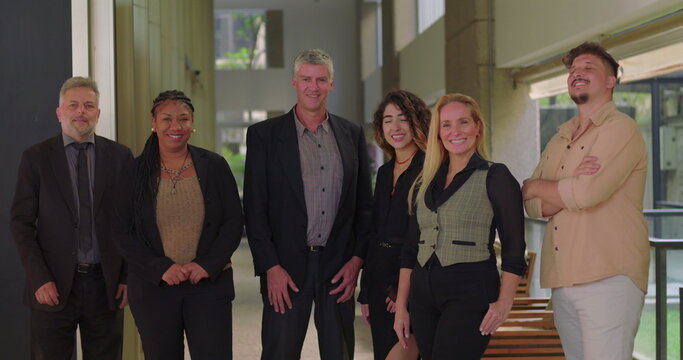 Corporate team smiling and standing together in office corridor, group of diverse professionals facing camera in relaxed and positive work environment - Powered by Adobe