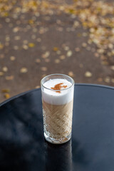 Latte in a tall glass against the backdrop of a cafe patio