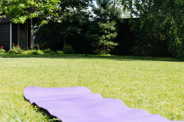 Purple yoga mat lying on grass in peaceful backyard garden on a bright sunny day, ready for exercise