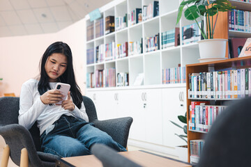 Asian woman using smartphone while relaxing in library lounge area