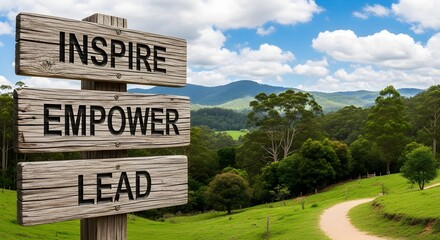 Wooden signpost reading 'inspire, empower, lead' on a countryside trail symbolizing coaching, mentoring, guidance and leadership direction.