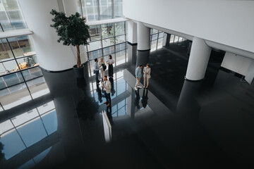 A small group of colleagues gathers in a bright, modern office lobby with glossy black floors, white columns, and expansive windows. They chat and share ideas in a stylish, open space.
