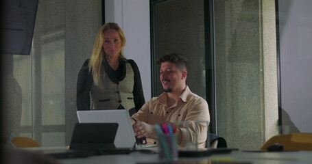 Coworkers celebrate success with cheerful high five in front of laptop during office meeting, smiling and standing together in modern workplace