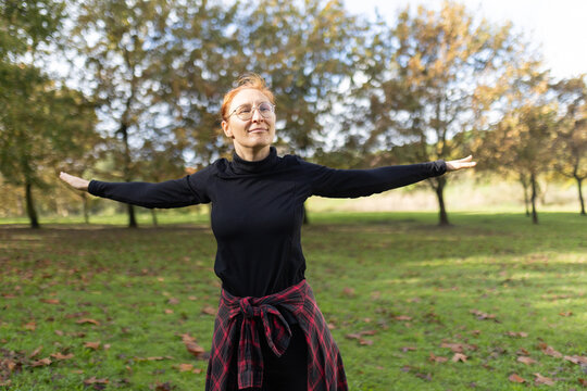 Redhead woman stretching arms experiencing freedom in park