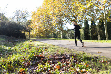 Woman jogging on park path during autumn day