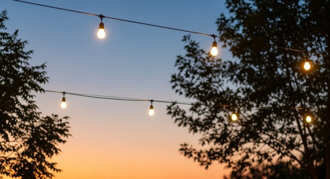 Serene evening scene with glowing string lights strung between silhouetted trees against a vibrant sunset sky in warm hues. Cozy, inviting atmosphere perfect for outdoor gatherings.