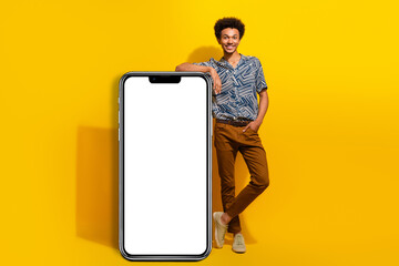 Cheerful young man leaning on a white panel against a yellow background, showcasing a stylish look and lively energy