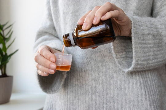 Woman pouring therapeutic liquid syrup into a dosage cup. Concept of fever relief, cough treatment, cold management, allergy prevention.