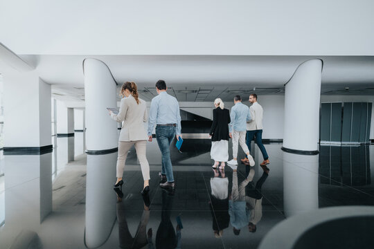 A group of colleagues stroll through a sleek, white and black office lobby, carrying tablets and folders. - Powered by Adobe