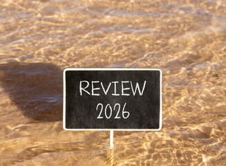Naklejka premium Review 2026 symbol. Concept words Review 2026 on beautiful black blackboard. Beautiful Red sea water background. Business and review 2026 concept. Copy space.